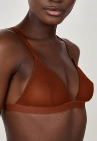 Bralette de triángulo marrón hecho de una tela texturizada, con delgadas correas ajustables y un borde de encaje en forma de conchas a lo largo de los bordes.