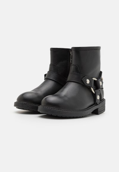 Musta nahkasaappaat nilkkapituudella, joissa on pyöreä kärki, sivuvetoketju ja koristeelliset hihnat hopeanvärisillä yksityiskohdilla. Mattapintainen viimeistely.