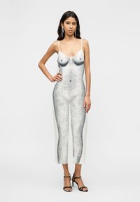 Γυναίκα που φοράει λευκό φόρεμα slip με λεπτομερή ασπρόμαυρο σκίτσο γυμνού γυναικείου σώματος, συνδυασμένο με μαύρα ψηλοτάκουνα σανδάλια.