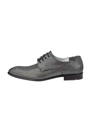 Chaussure habillée à motif noir et blanc, avec un design épuré, une surface lisse et un talon bas. Elle comporte six œillets et un bout arrondi.