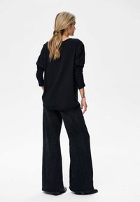 Zwarte lange mouwen top met een ontspannen pasvorm, gecombineerd met wijde zwarte denim broeken. Minimalistisch ontwerp, gladde textuur en subtiele stikseldetails.