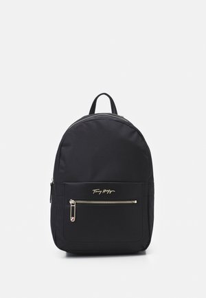 Czarny plecak z przednią kieszenią na zamek i złotym logo Tommy Hilfiger na jednolitym białym tle.