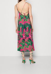 Maxi šaty s jasně růžovým pozadím a zelenými tropickými listovými vzory, s nízkým otevřeným zadním dílem a tenkými nastavovacími ramínky. Nosit se zelenými podpatky.