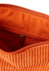Custodia arancione in corduroy con zip, presenta un esterno testurizzato, una fodera interna liscia e una tasca con zip più piccola per lo stoccaggio.