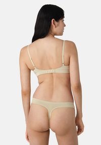 Conjunto de sujetador y tanga beige, con tirantes ajustables y cierre de gancho. Textura suave con un detalle mínimo. Vista trasera mostrada.