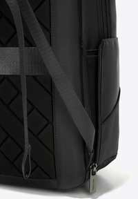 Zaino nero con superficie testurizzata e motivo a diamante, dotato di cerniere e spallacci regolabili realizzati in tessuto resistente.