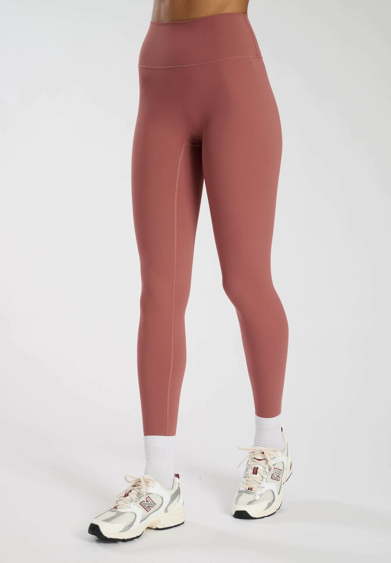 Hoge taille, aansluitende leggings in stofroze met een gladde textuur en ton-sur-ton stiksels, gecombineerd met witte sokken en sneakers.