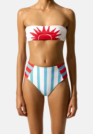 Kobieta w bikini bez ramiączek z czerwonym motywem słońca na górze i wysokim stanem spodni z niebieskimi paskami i czerwonymi bocznymi panelami.