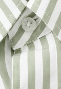 Prim-plan al gulerului unei cămăși cu dungi verticale verde deschis și alb, cu un nasture transparent prins în găura nasturelui.