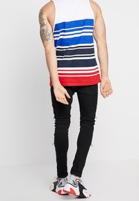 Vit tanktopp med horisontella röda, blå och marinblå ränder, kombinerad med svarta skinny jeans och flerfärgade sneakers.