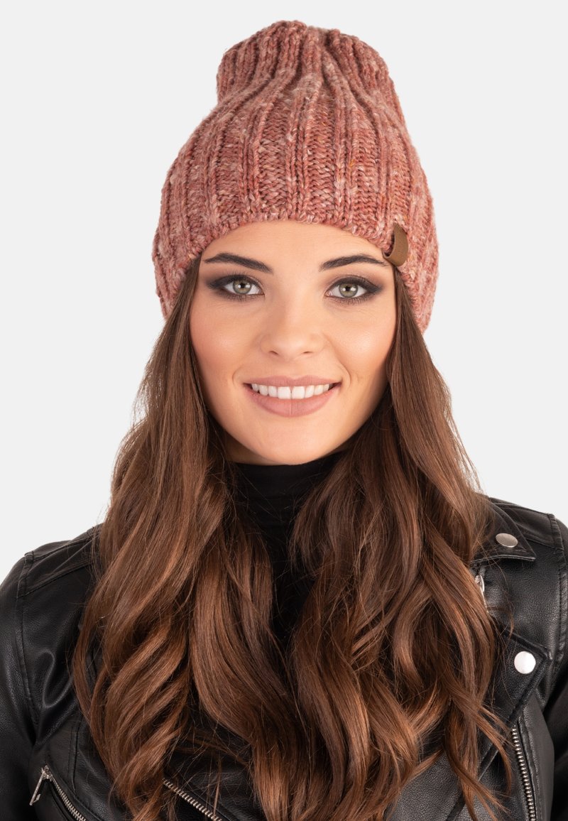 Gorro de punto en un cálido color rojo-rosado con una textura acanalada y un pequeño tag de cuero marrón como acento. Diseñado para un ajuste ceñido.