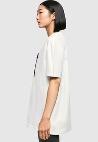 White cotton t-shirt with a relaxed fit, featuring short sleeves and a graphic print on the front. Smooth texture, hip-length design.