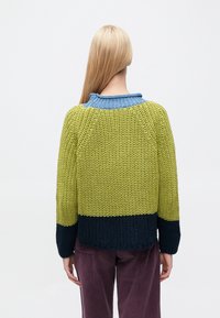 Megztinis su spalvų blokų dizainu, kur domina žalios, mėlynos ir tamsiai mėlynos juostos. Tekstūruota medžiaga, apvalus kaklas ir ilgos rankovės.