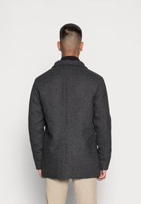 Šedý kabát z vlněné směsi s herringbone vzorem, s klopami a jediným rozparkem na zadní straně. Nabízí přiléhavý střih a minimalistický design.