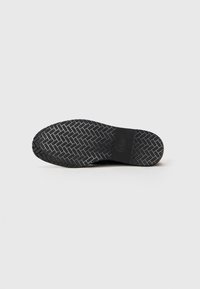 Semelle de chaussure noire avec un motif en chevron et une section centrale lisse affichant les détails de la marque et de la taille.
