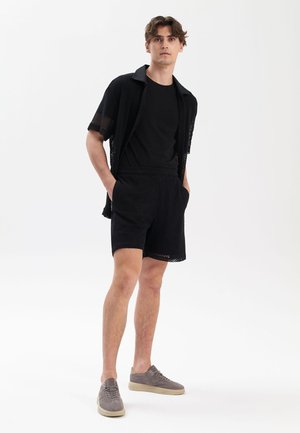 Czarna siateczkowa koszulka z krótkim rękawem na czarnej koszulce, zestawiona z czarnymi szortami. Szare buty o teksturowanej zamszowej powierzchni. Prosty, nowoczesny design.