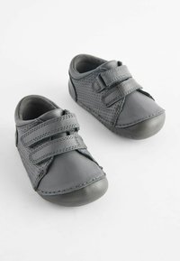 Chaussures en cuir grises avec deux bandes Velcro, bout rond, design perforé sur les côtés et semelles en caoutchouc pour la durabilité.