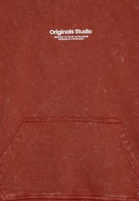 Svetrová mikina v hrdzavej farbe s fleece štruktúrou, predné vrecko a bielou potlačou loga "Originals Studio" s detailmi značky nad ním.
