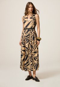 Maxi dress vaale beige värviga, mustade lehepiltidega, ilma varrukateta disain, V-kujuline kaelus, kergelt kitsenev talje ja voogav seelik. Rihmadega must vööd rõhutab.