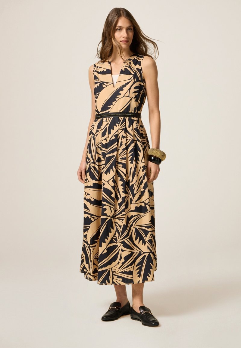 Maxi dress vaale beige värviga, mustade lehepiltidega, ilma varrukateta disain, V-kujuline kaelus, kergelt kitsenev talje ja voogav seelik. Rihmadega must vööd rõhutab.