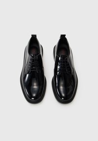 Chaussures à lacets en cuir verni noir avec une finition lissée, bout rond et semelle en caoutchouc texturé contrastant. Avec une languette au talon.