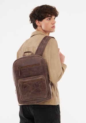 Brown leather backpack with two zippered front pockets, a top handle, and an adjustable strap. Smooth texture with a worn appearance.
