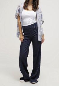 Lätt blommig kimono i blått och vitt över en figursydd vit linne, kombinerad med mörka vida byxor och vita sneakers.