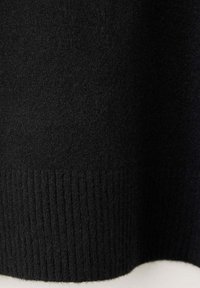 Gros plan d'un tissu tricoté noir montrant une texture douce et un ourlet côtelé au bord inférieur.