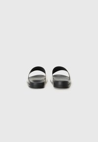 Sorte åpne sandaler med minimalistisk design, som har glatte materialer, en lavprofil fotbed og buede stropper for fotstøtte.