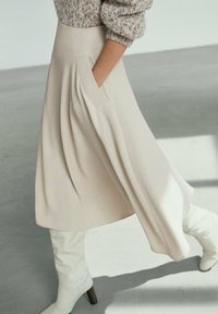 Crème-kleurige, knielange rok met een losse pasvorm en zijzak, gecombineerd met witte kniehoog laarzen en een gestructureerde trui.