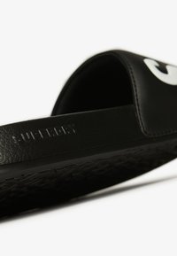 Zwarte slide-sandaal met een gematteerde, getextureerde bovenkant met een groot wit logo. Getextureerde zwarte zool ontworpen voor grip. "SUPERDRY" in reliëf op de band.