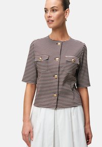 Bruin en witte gestreepte blouse met korte mouwen, voorzien van gouden knopen en twee borstzakken. Gestyled met een witte rok.
