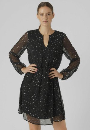 Robe noire avec des manches transparentes, présentant un décolleté en V et une taille élastique. Agrémentée de pois argentés sur l'ensemble.