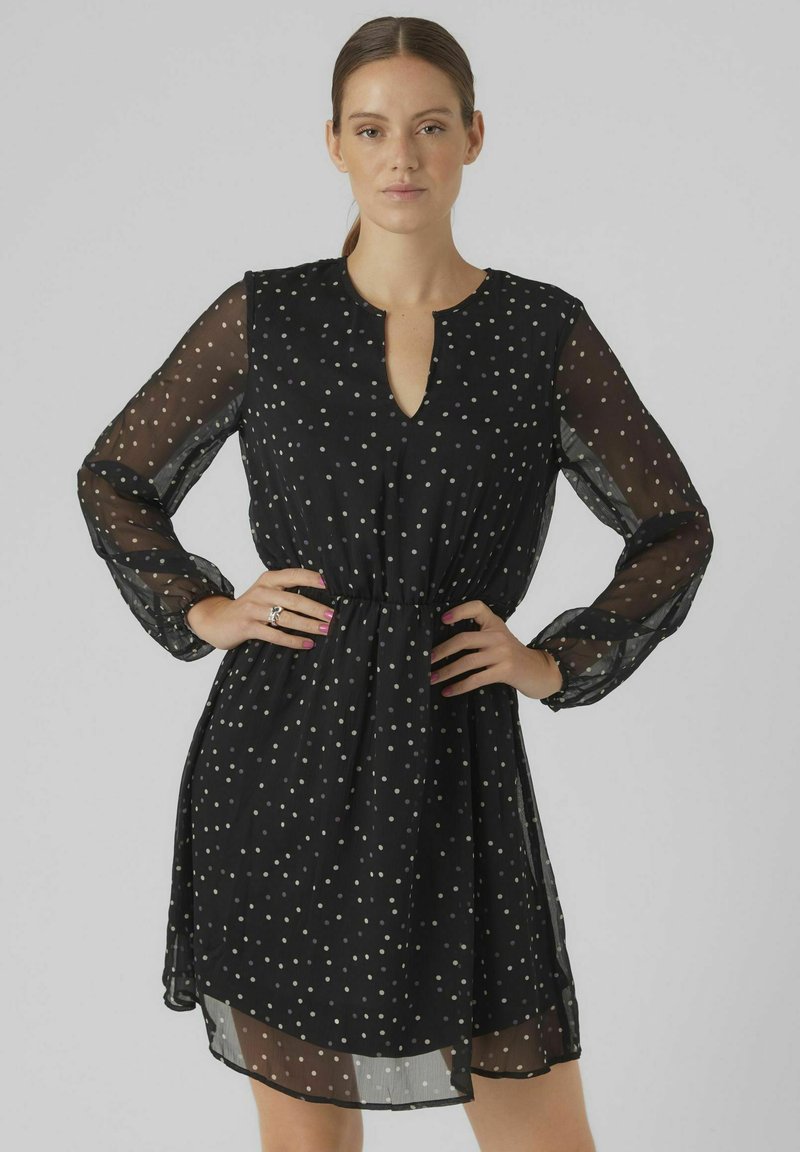 Robe noire avec des manches transparentes, présentant un décolleté en V et une taille élastique. Agrémentée de pois argentés sur l'ensemble.