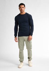 Mörkblå långärmad tröja med rund hals, kombinerad med ljus olivfärgade cargobyxor med sidofickor, elastiska muddar och krämfärgade sneakers.