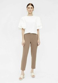 Haut blanc à manches courtes avec des volants superposés, associé à un pantalon marron ajusté et des sandales à talons blocs beiges. Design simple et moderne.