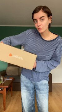 Brun pappeske med Zalando-logo vist. Modell iført en blå og hvit stripete langermet skjorte og lyseblå slitte jeans.