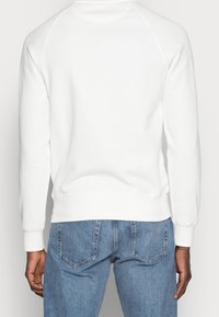 Sudadera blanca con cuello redondo y mangas raglán, con puños y dobladillo de canalé, combinada con unos jeans de mezclilla azul claro.