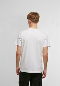 Hvid bomulds T-shirt med korte ærmer og rund halsudskæring, båret med sorte cargo bukser. Enkel, uprydet design, glat tekstur.