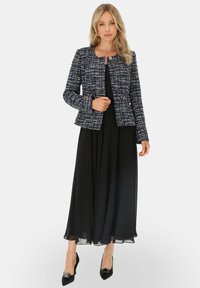 Granatowa marynarka z tweedu o dopasowanym kroju, okrągłym kołnierzu i zapięciu na guziki, zestawiona z długą czarną zwiewną sukienką i czarnymi szpilkami.