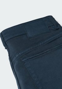 Poche arrière d'un jean denim bleu marine foncé avec des coutures visibles et un patch rectangulaire en cuir de la marque à la ceinture.