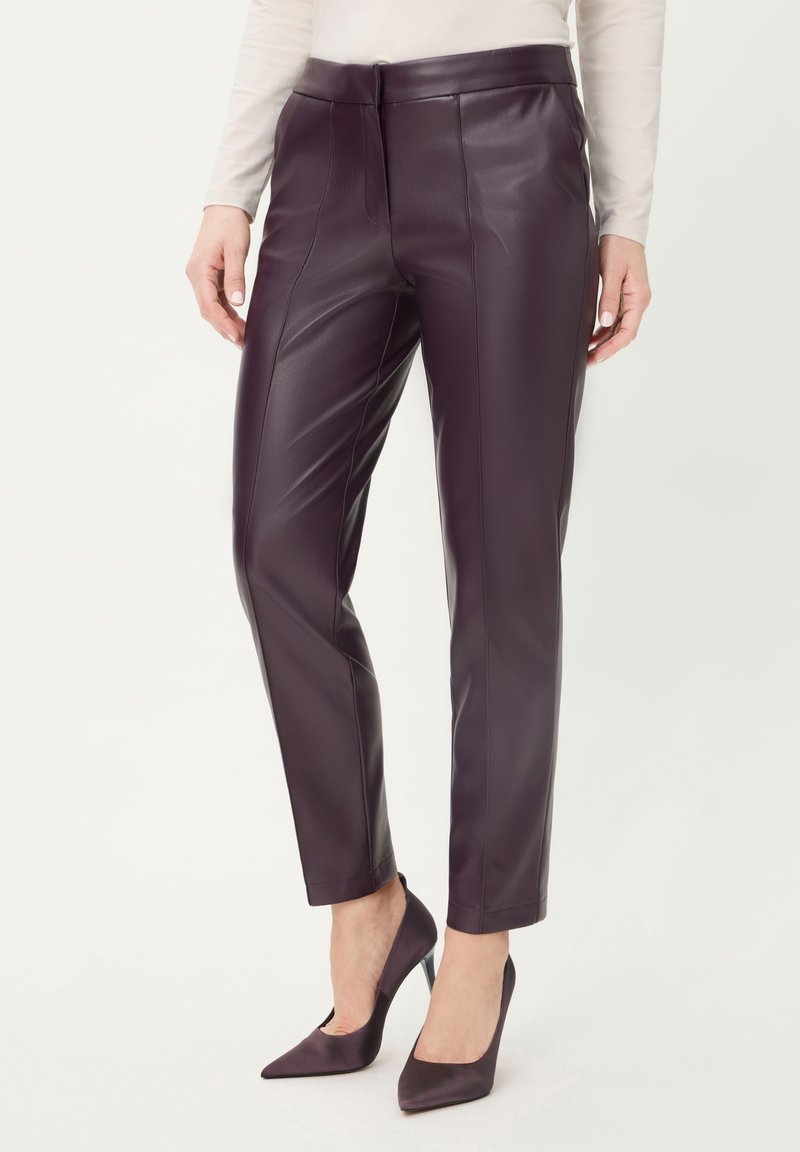 Woman wearing slim-fit, dark purple leather pants paired with matching pointed high-heeled shoes and a light beige long-sleeve top.