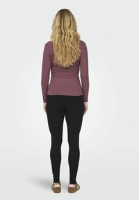Csíkos, hosszú ujjú mauve felső fekete leggingsszel és barna szandállal párosítva. A haj hullámos, a hát közepéig ér. Világos, sima háttér.