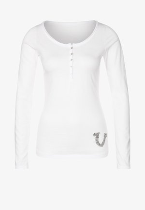 Witte damesblouse met lange mouwen, ronde hals, vijf knopen aan de voorkant en een klein grijs patroon vlak bij de zoom aan de linkerkant.