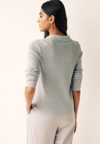 Pulover gri deschis cu model în dungi, cu guler, design ajustat și mâneci ușor evazate, purtat peste pantaloni deschisi la culoare.