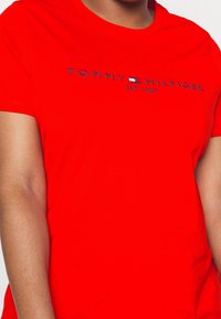 Rød bomulds T-shirt med rund halsudskæring og korte ærmer. Centreret logo i marineblå: "TOMMY HILFIGER EST. 1985" med en lille flagdetalje.