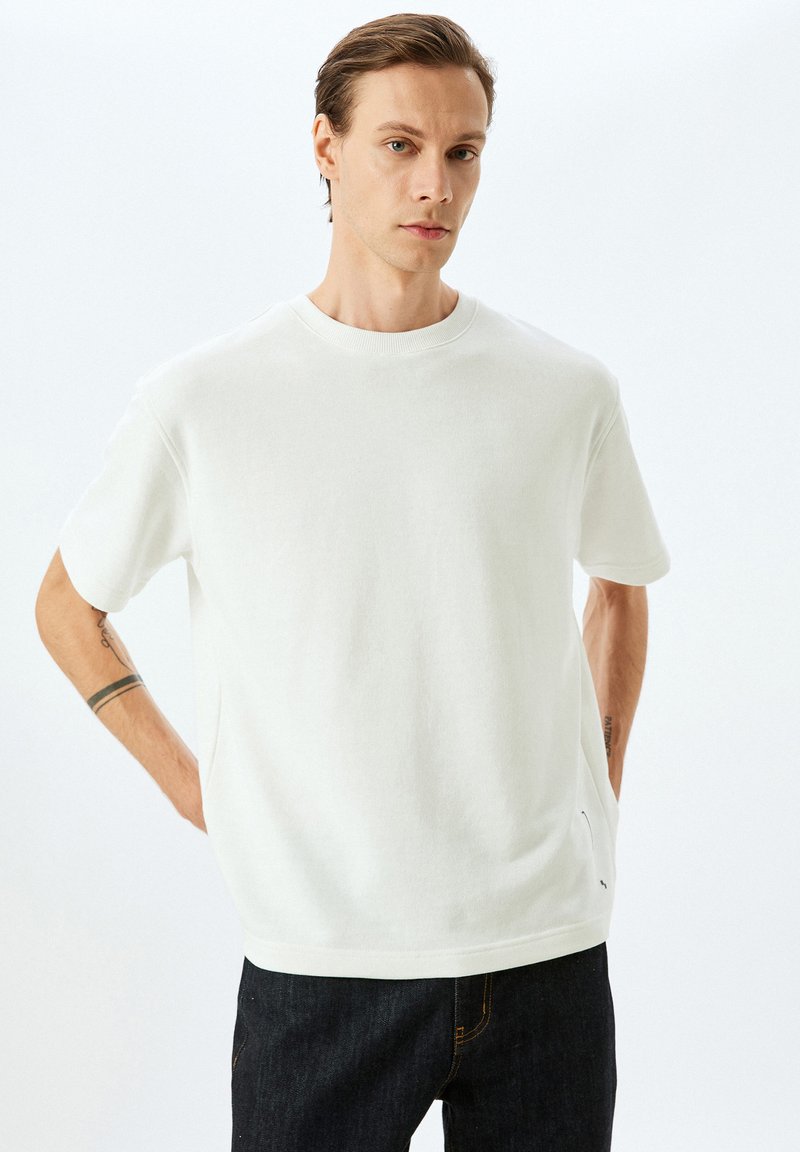 Hvid bomulds t-shirt med korte ærmer, rund halsudskæring, afslappet pasform og subtile sidesøm detaljer. Parret med mørk denim jeans.