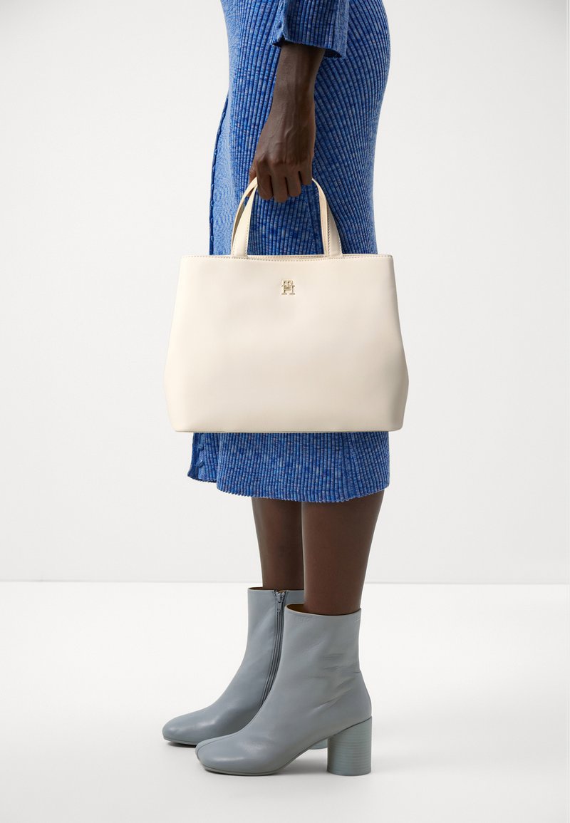 Beige Leder Tote-Bag mit zwei Griffen und einem goldenen Logo, kombiniert mit einem blauen gerippten Kleid und hellgrauen Stiefeletten mit einem klobigen Absatz.