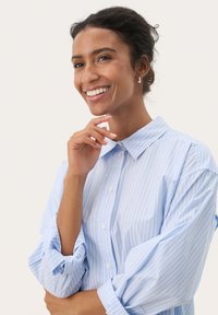 Camicia button-up a righe blu chiaro con colletto, vestibilità rilassata e maniche lunghe arrotolate. Tessuto liscio, lucentezza sottile e design classico.