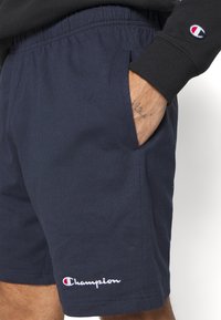 Pantalones cortos Champion en azul marino hechos de una mezcla de algodón, con una cinturilla elástica, bolsillos laterales y detalle del logotipo bordado.